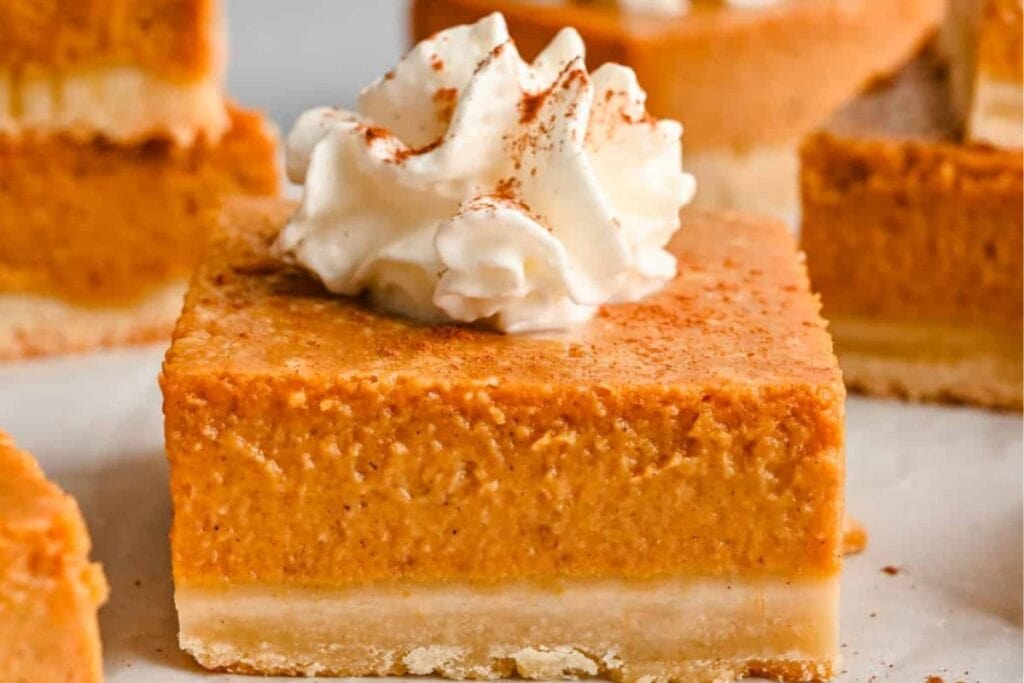 Pumpkin pie bars topped with whipped cream and dusted with cinnamon.