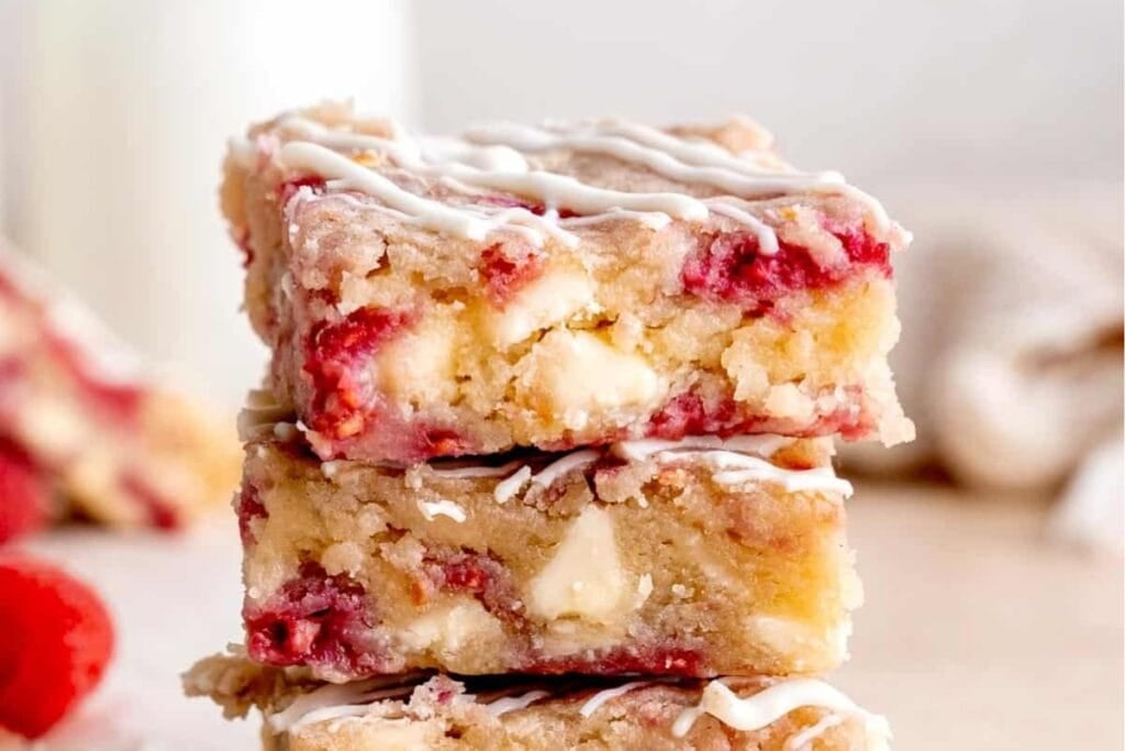 Raspberry and white chocolate blondie bars stacked on a table.