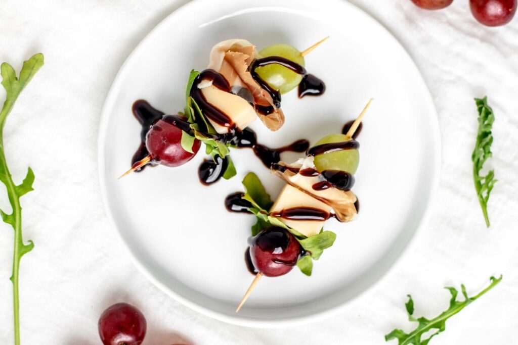 Grape gouda arugula skewers on a white plate.