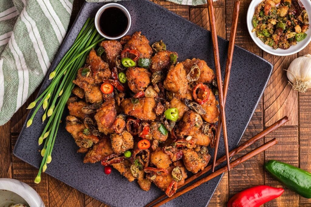 Salt and pepper pork chop bites served on a square black plate with chopsticks.