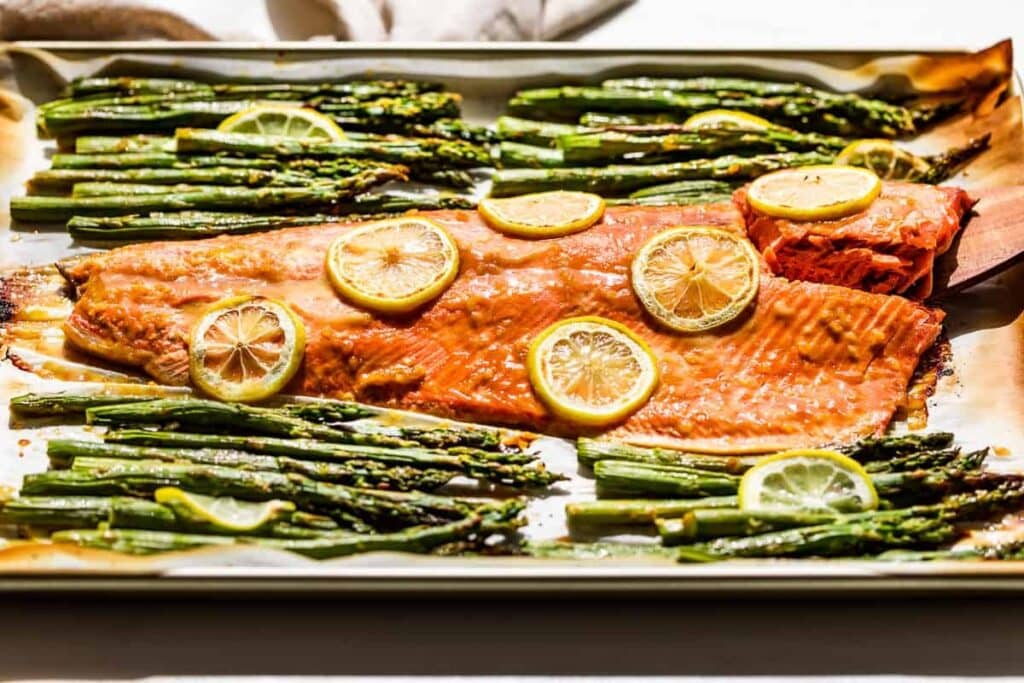 Baked salmon and asparagus on a sheet pan with lemon slices.