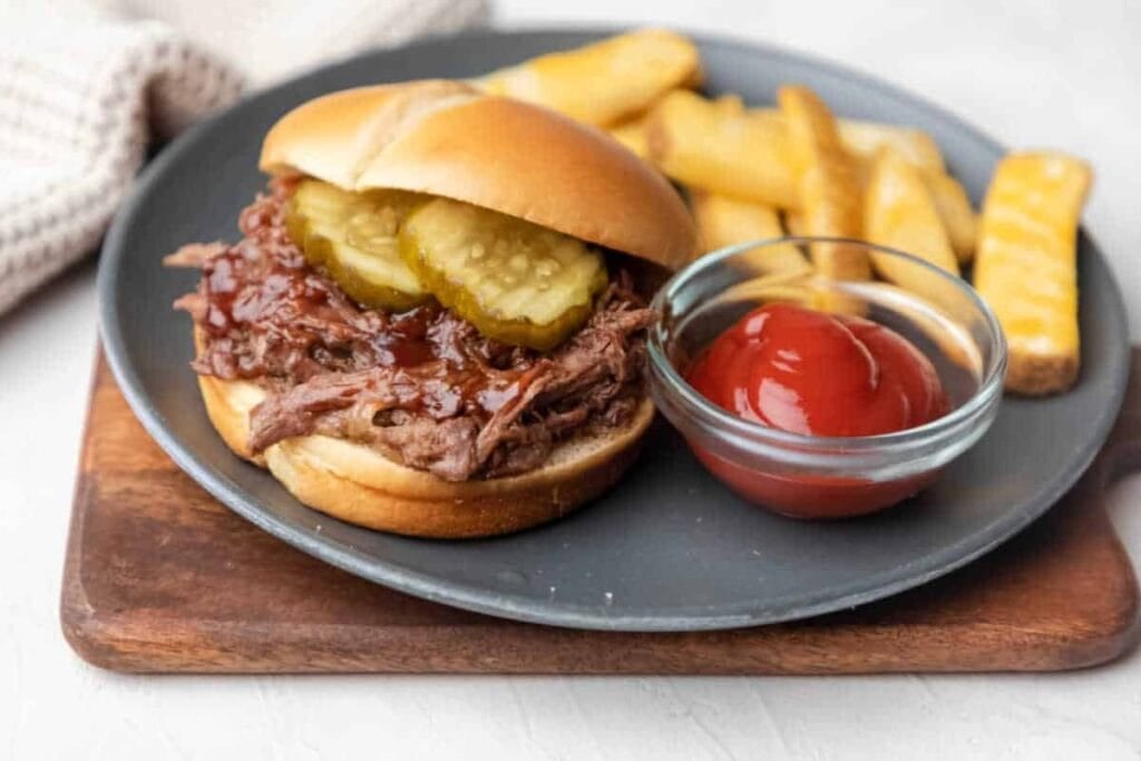Slow cooker barbecue beef sandwich served with fries and ketchup on a plate.
