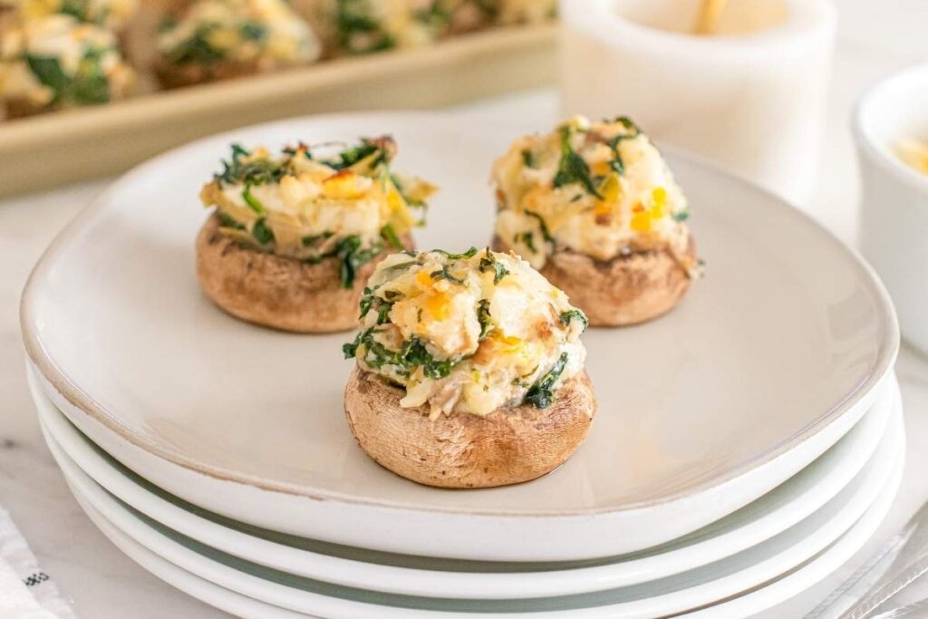 Spinach artichoke stuffed mushrooms served on a white plate.