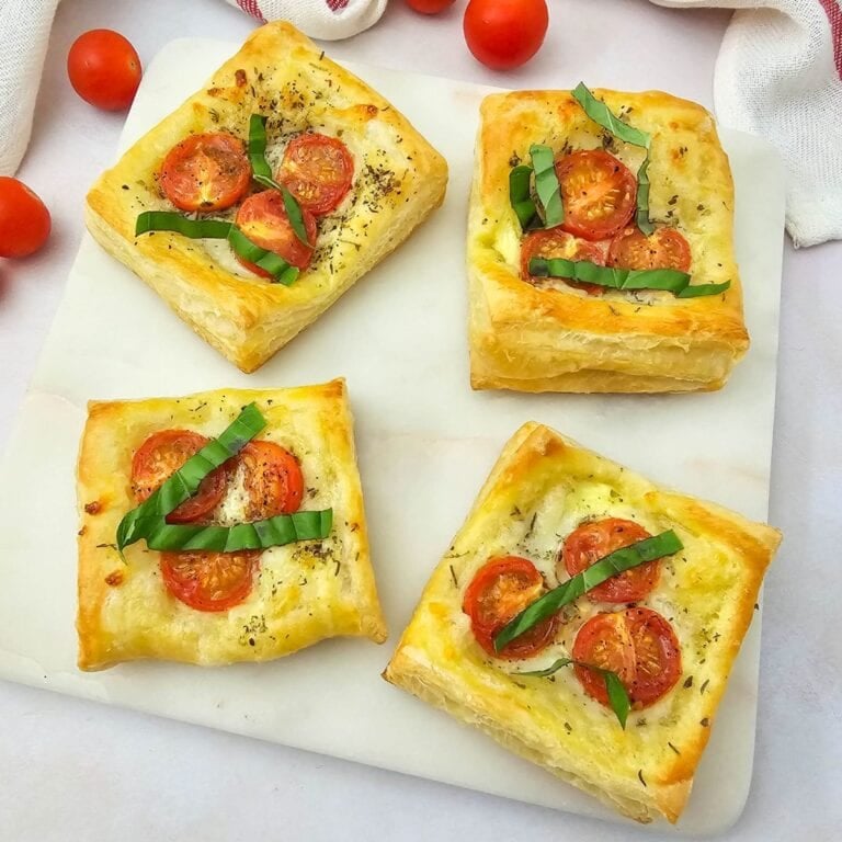 Golden tomato puff pastry tartlets topped with herbs on a serving plate.