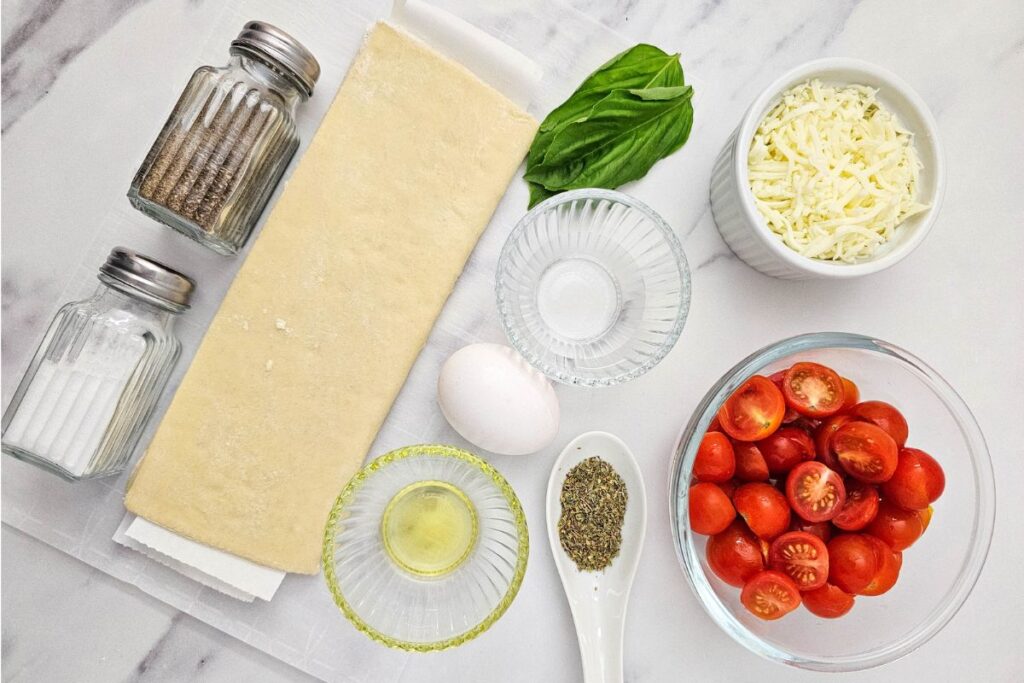 Ingredients for tomato puff pastry tarts arranged on a table.