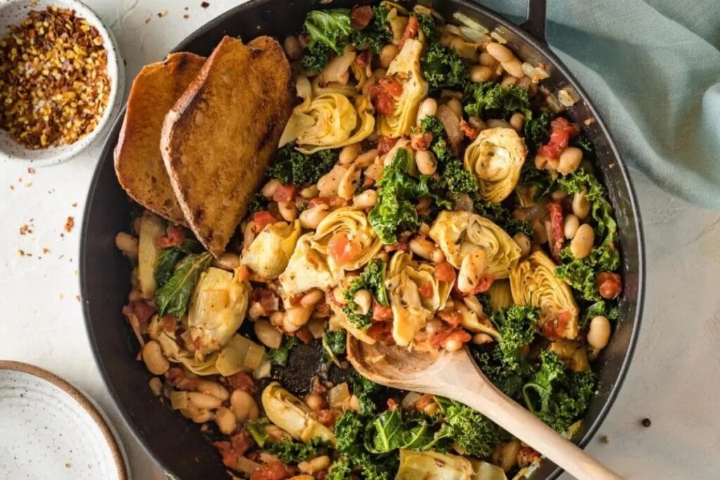 Tuscan white beans with vegetables and crusty bread in a skillet.