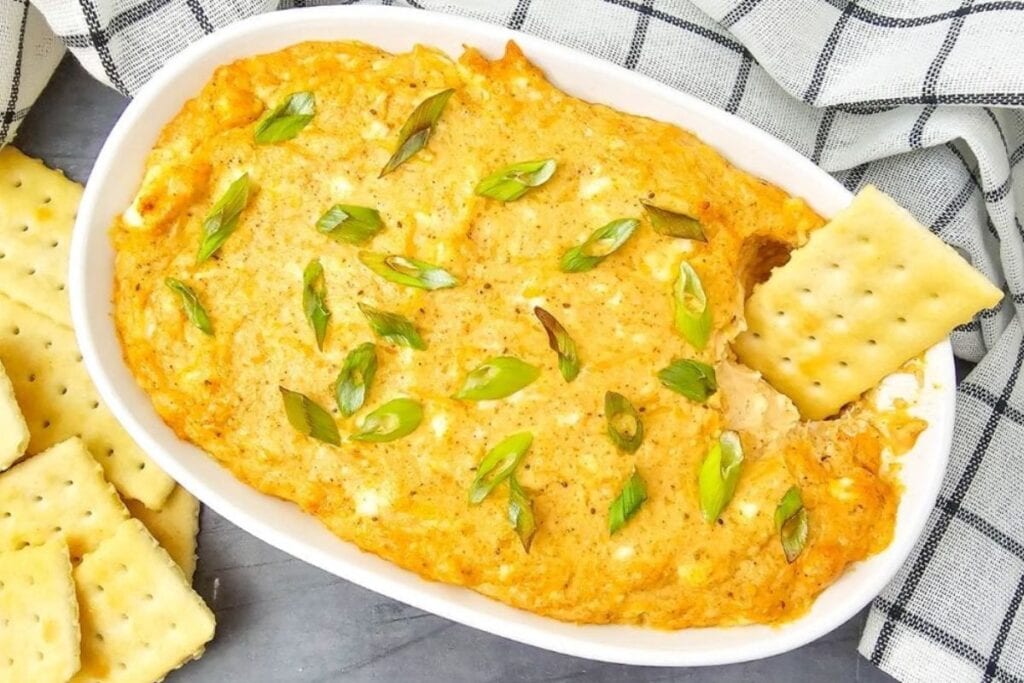 Hot crab dip in a rectangular baking dish served with crackers.