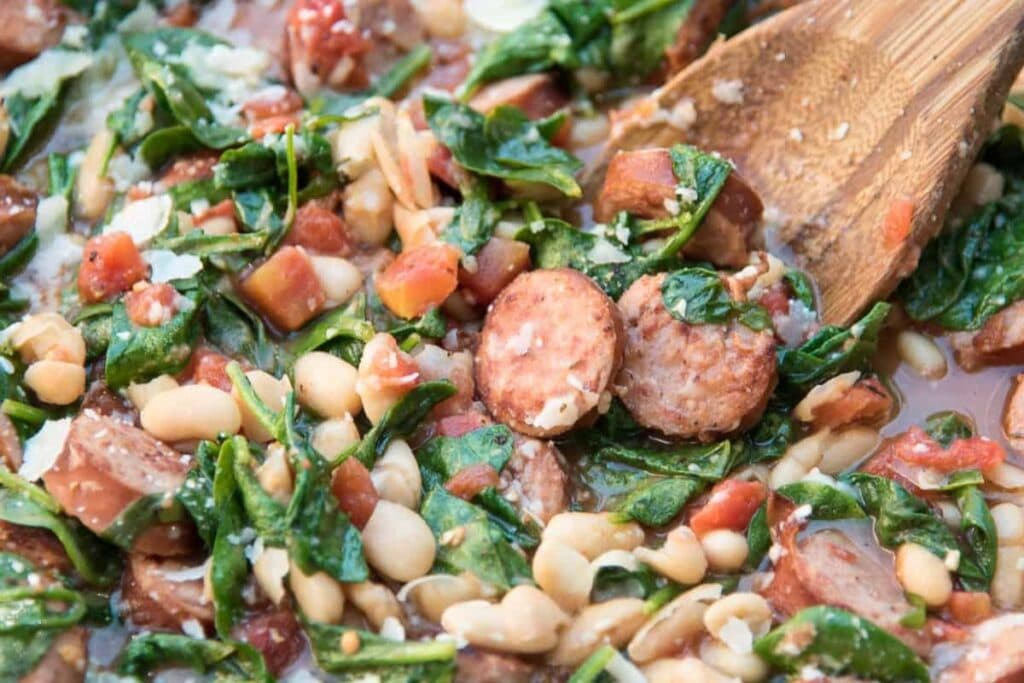 A close up shot of sausage and white beans with spinach.