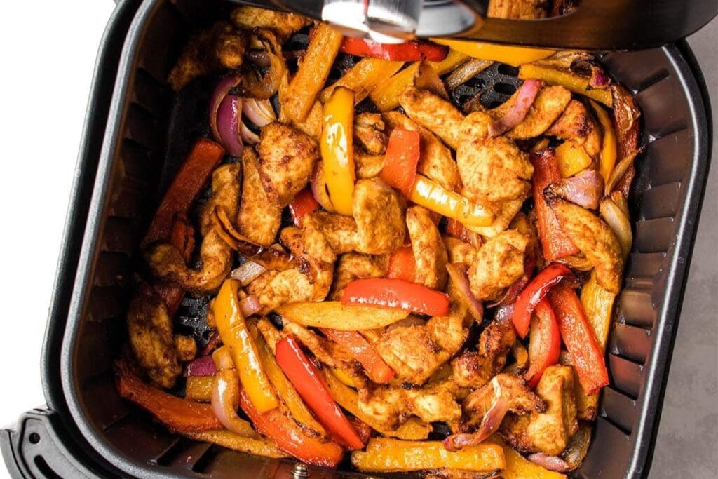 Chicken fajitas with bell peppers and onions cooking in an air fryer basket.
