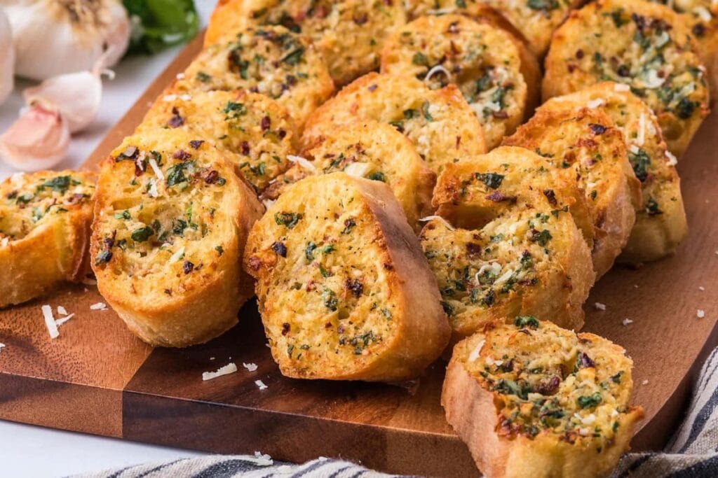 Slices of Air Fryer Garlic Bread on a wooden board, golden and crispy with herbs