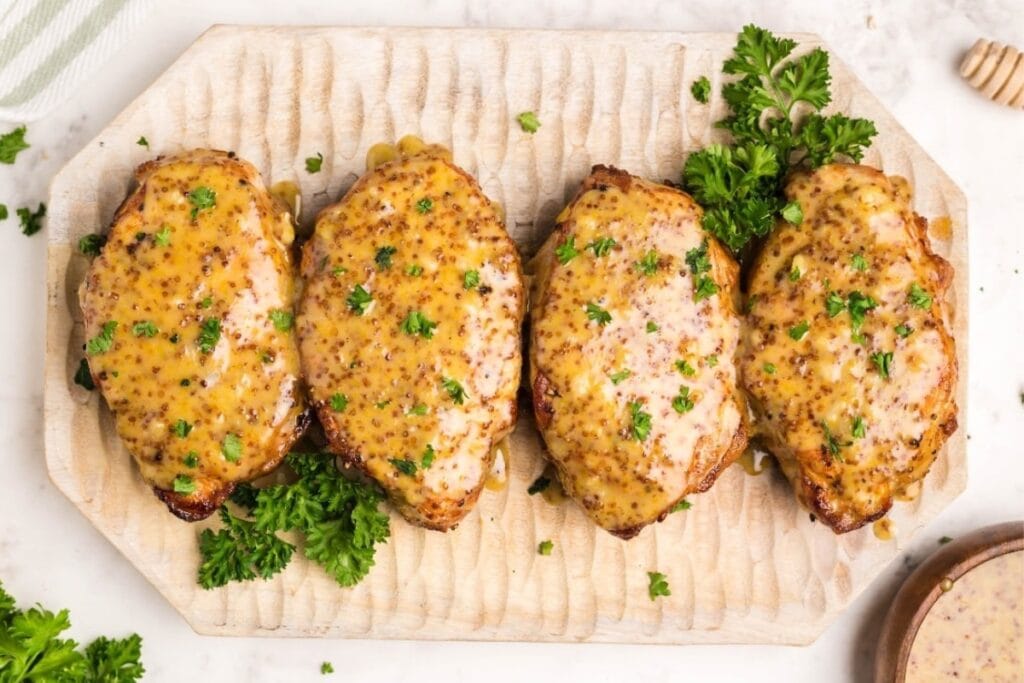 Honey mustard pork chops served on a wooden board, garnished with herbs.