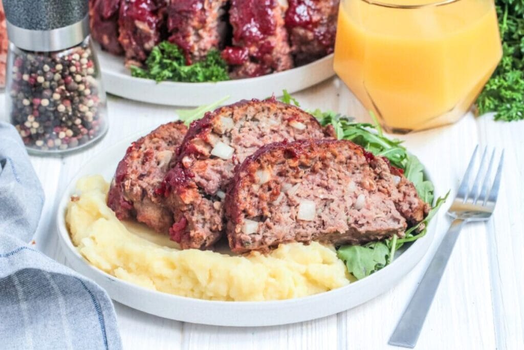 Meatloaf on a white plate served with mashed potatoes.