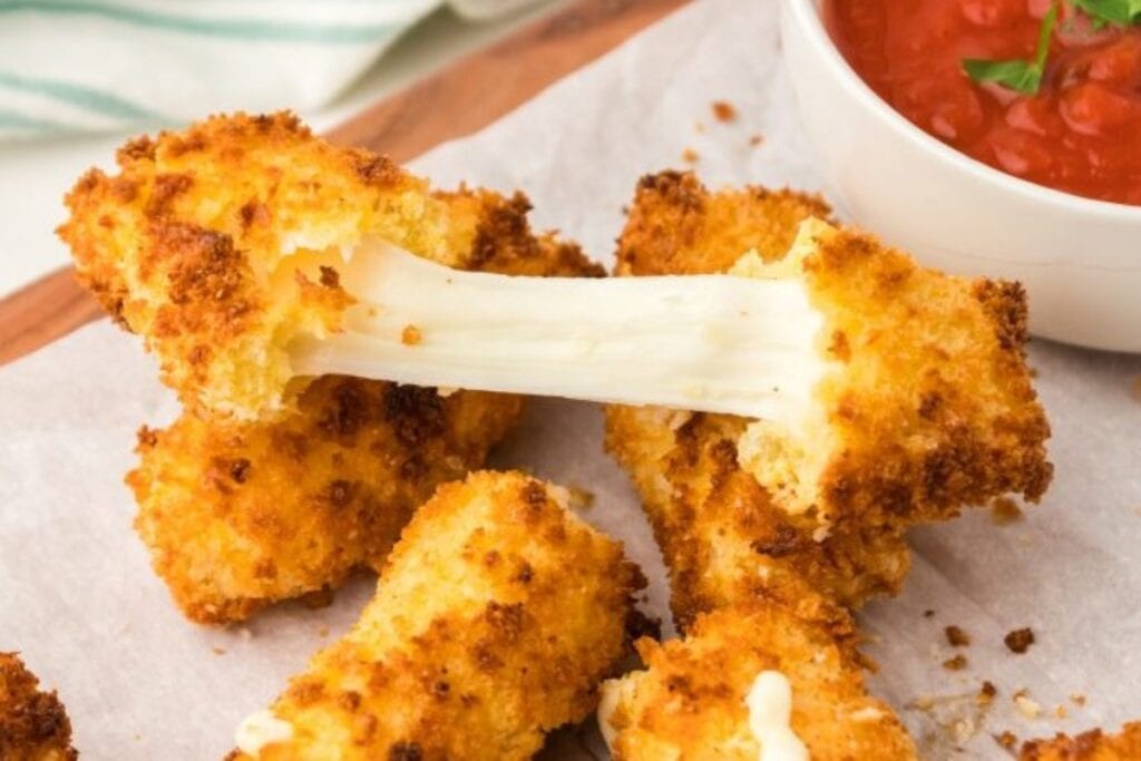 Air-fried Mozzarella Sticks on a wooden board lined with parchment paper.