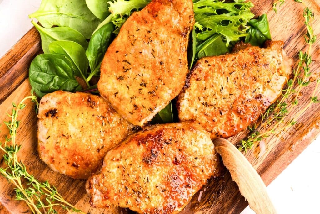Pork chops served on a wooden board.