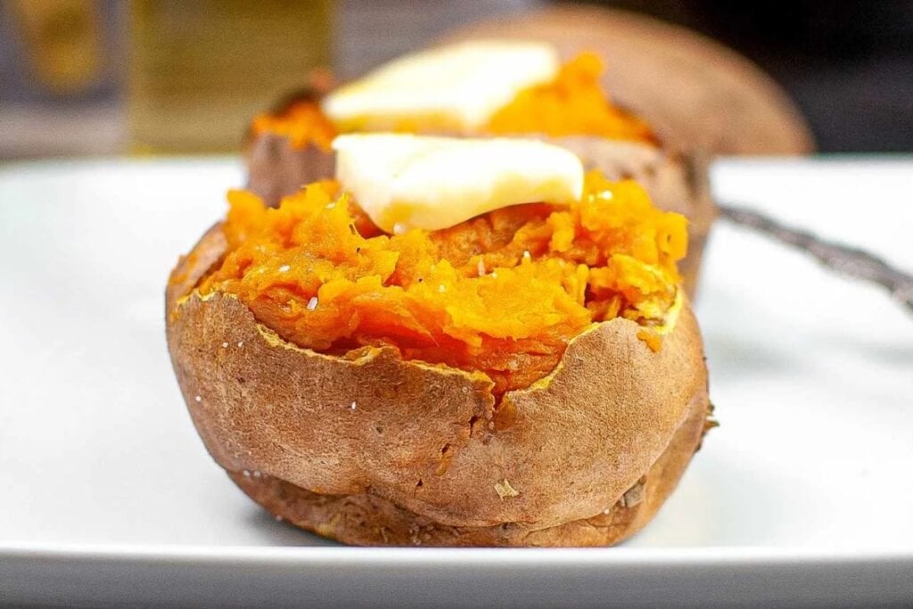 Air fryer sweet potatoes topped with butter on a white plate.