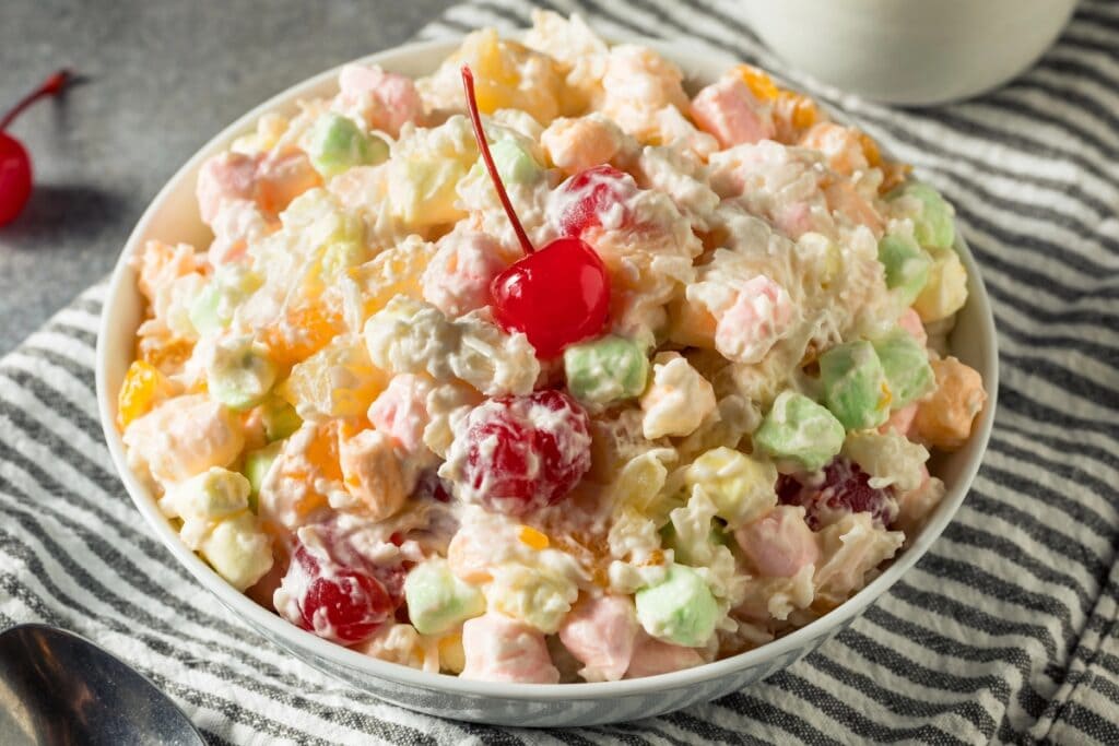 Ambrosia salad in a white bowl, topped with a cherry.