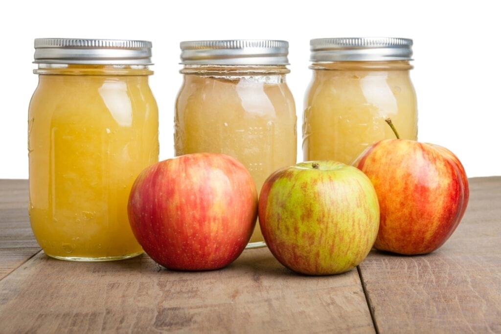 hree jars of applesauce with fresh red apples placed in front.