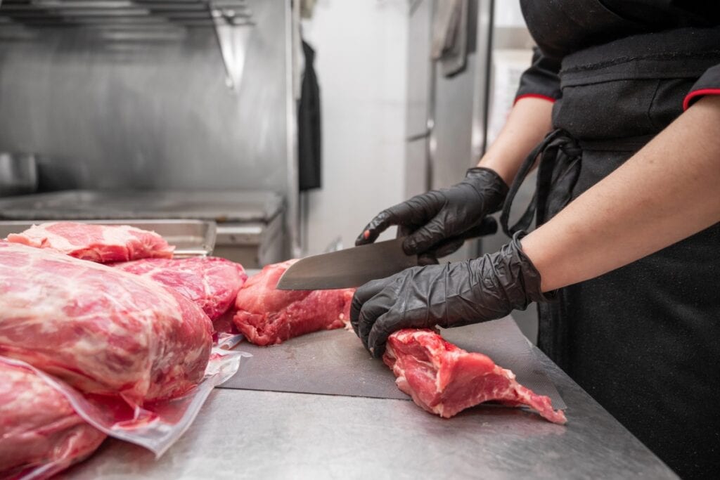 Female butcher slicing meat with a knife.