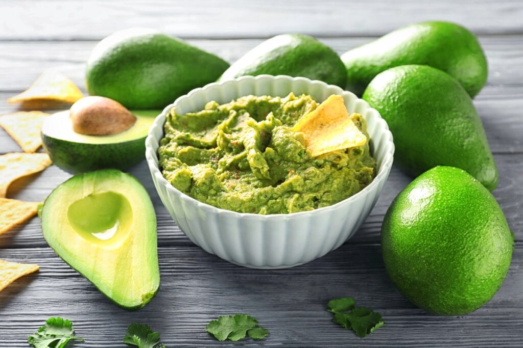 Avocados on a table with mashed avocado in a bowl.
