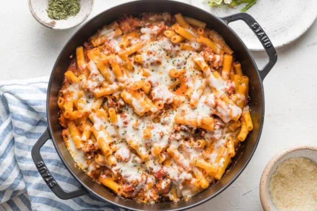 Baked ziti in a black skillet, topped with melted cheese.