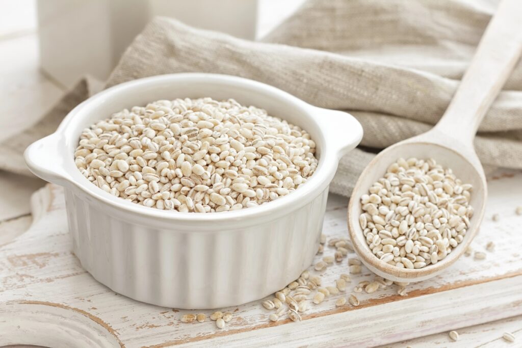 Barley pearls in a white bowl and on a wooden spoon.