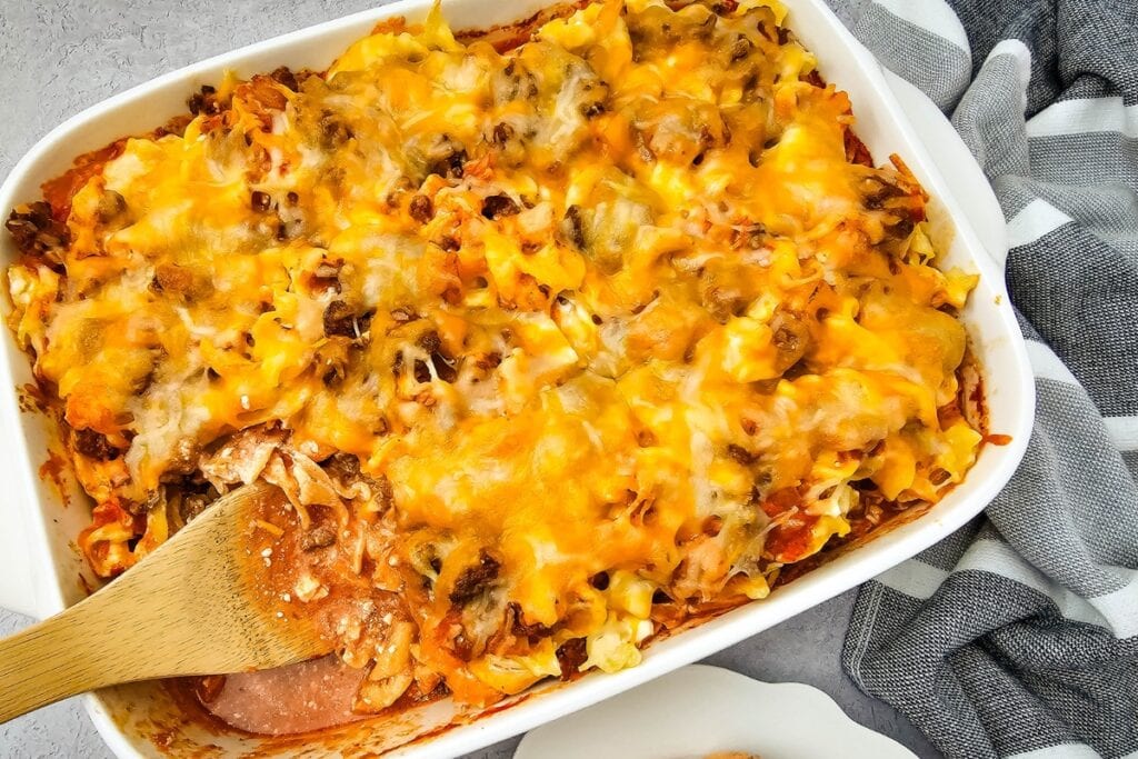 Beef noodle casserole in a white baking dish with a wooden spoon.