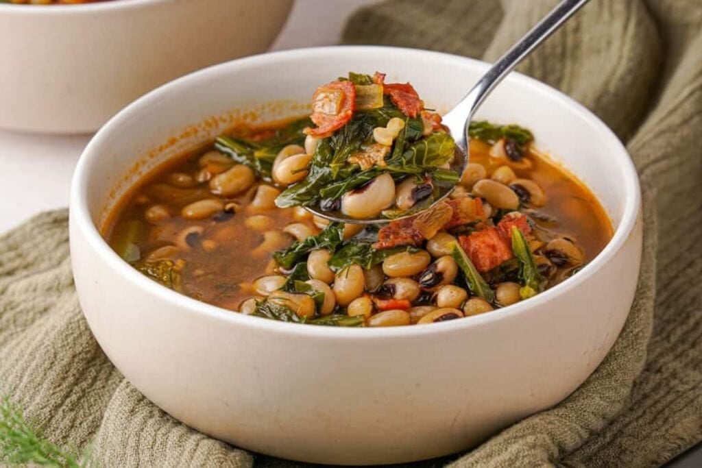 Black-eyed peas and greens scooped with a spoon in a white bowl.