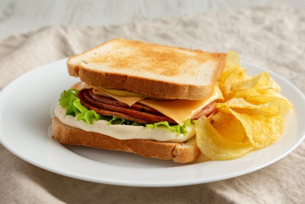 Bologna sandwiches on a white plate with chips on the side.
