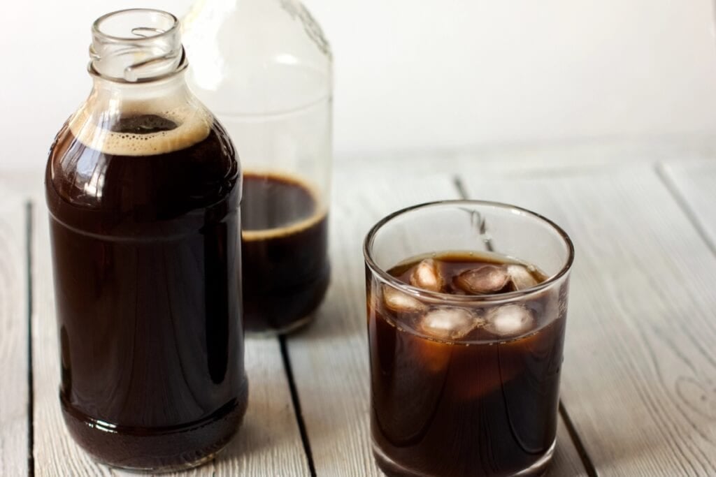 A glass bottle of cold brew next to a filled glass with ice.