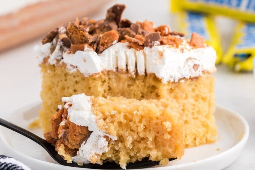 Butterfinger Poke Cake lifted by a fork from plate.