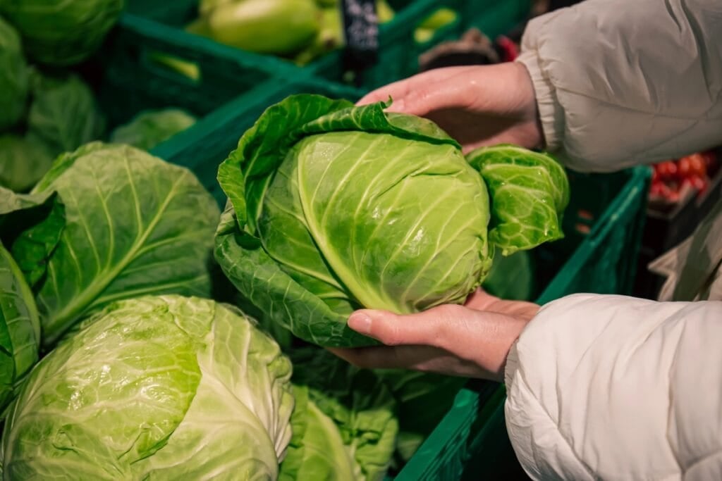 Woman holding a cabbage in a grocery store produce section.