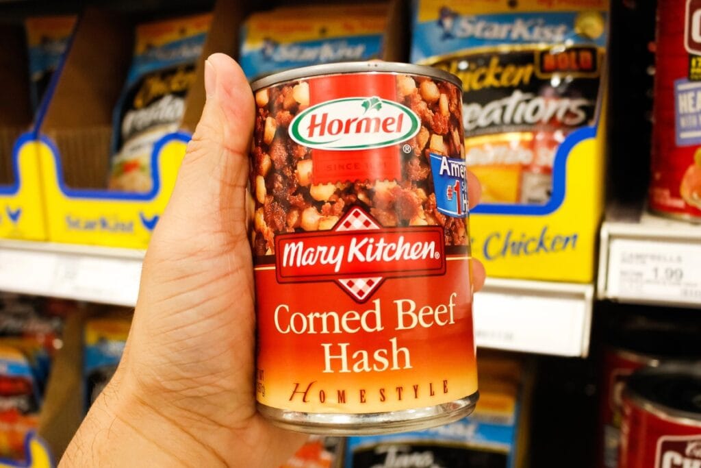 Hand holding a can of corned beef hash in a grocery store.