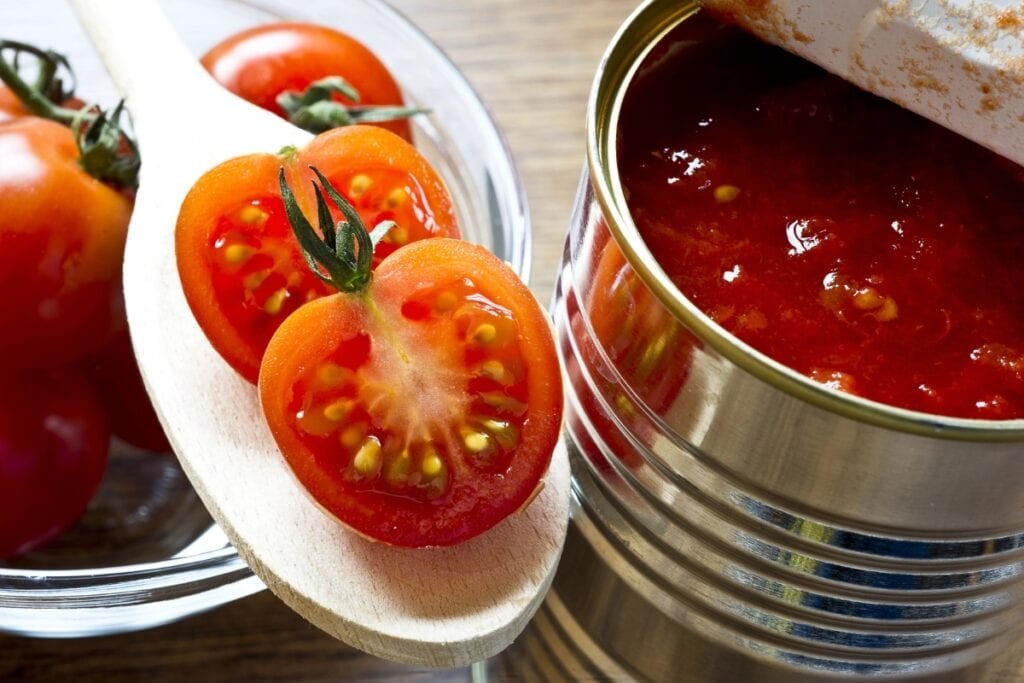 Canned tomato and fresh tomato on a table.