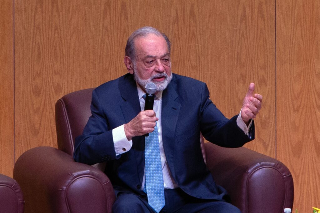 Carlos Slim Helu speaking into a microphone while seated on a chair.