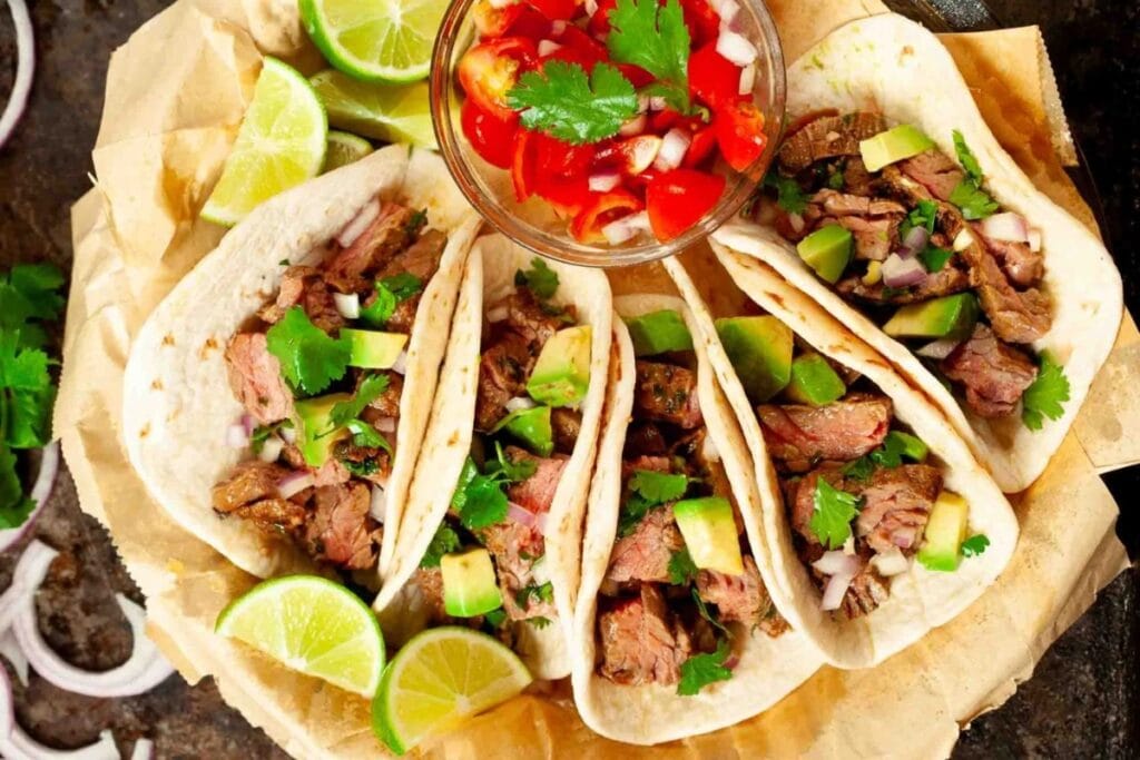 Carne asada tacos served with lime wedges and a bowl of fresh salsa.