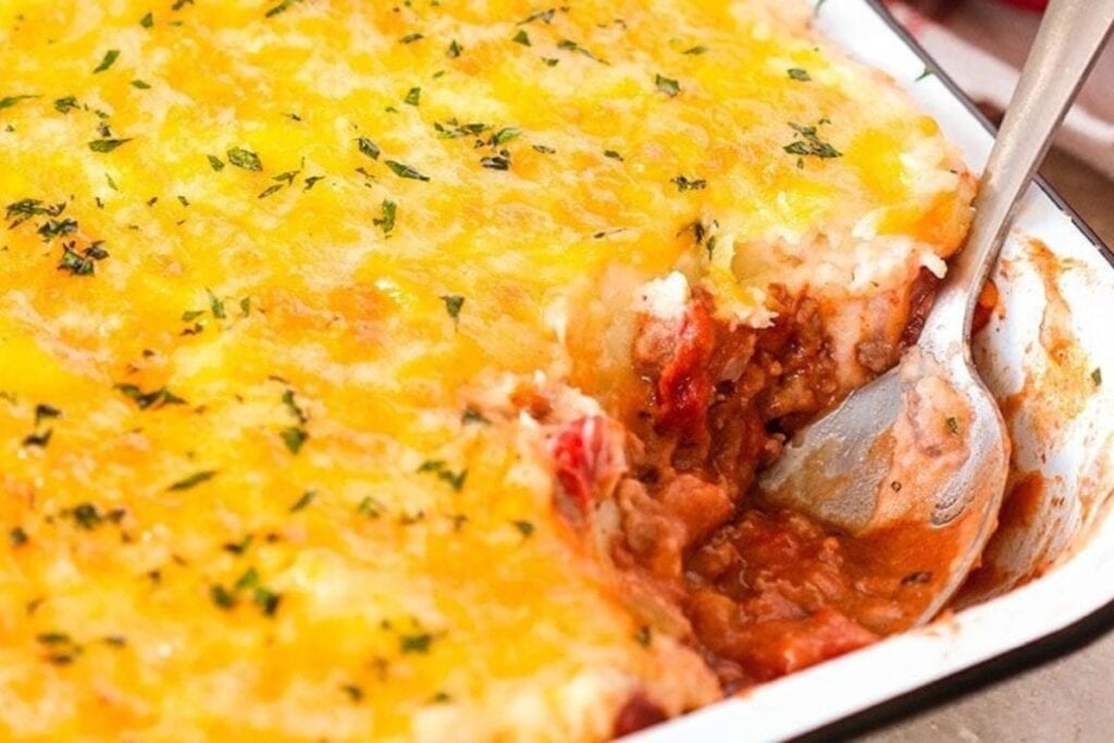 Cheesy mashed potato casserole in a baking dish with a spoon.