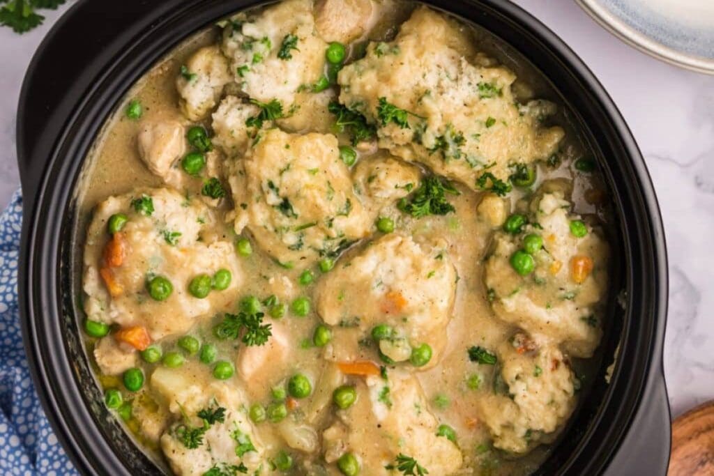 Chicken and dumplings in a black bowl.