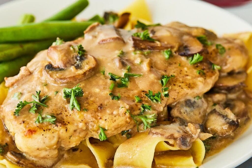 Chicken Marsala with mushrooms and parsley over pasta, served on a plate.