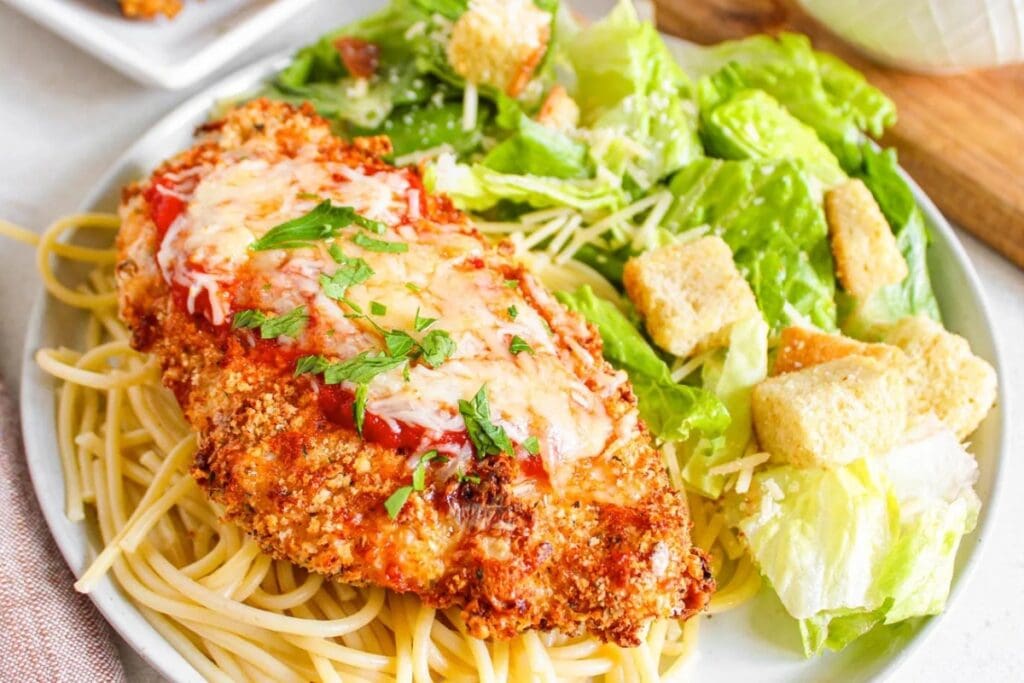 Chicken Parmesan served with pasta and vegetables on a plate.
