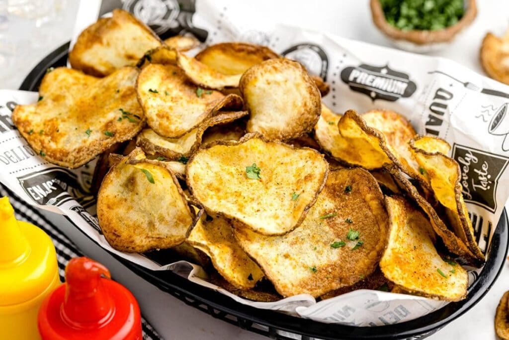 Potato chips in an oval plastic basket lined with parchment paper.