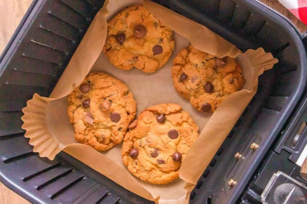 Chocolate chip cookies in an air fryer lined with parchment paper.