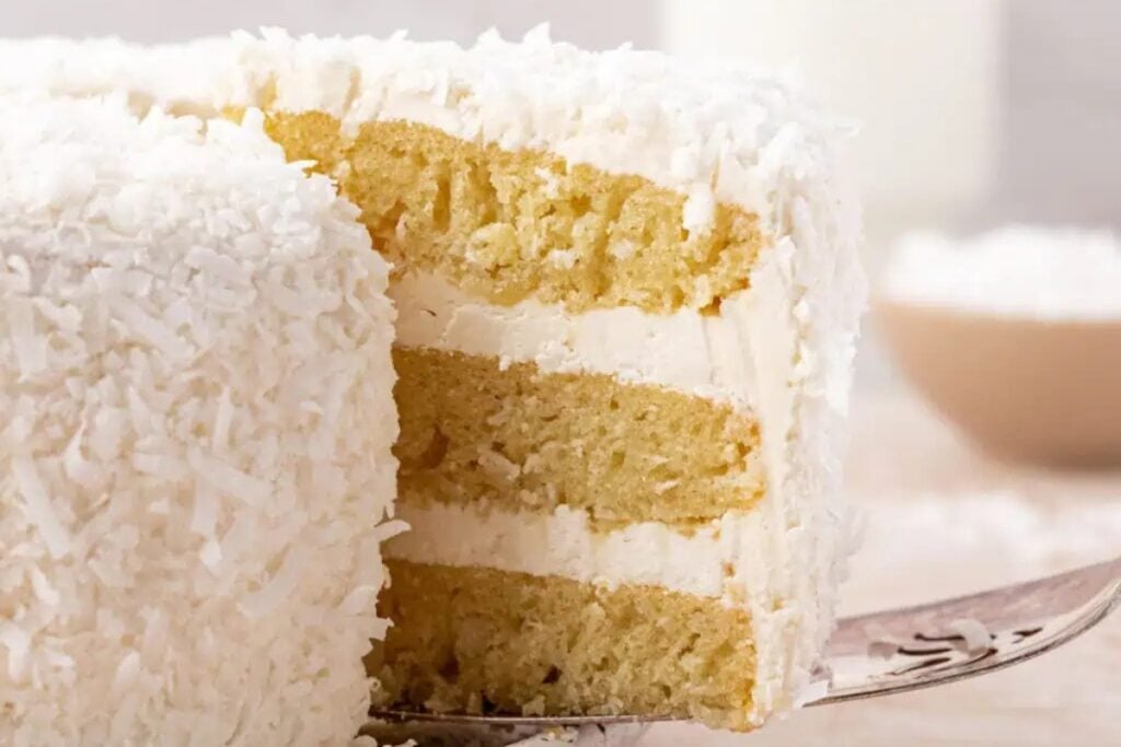 Whole coconut cake with a slice removed, showing the inside.
