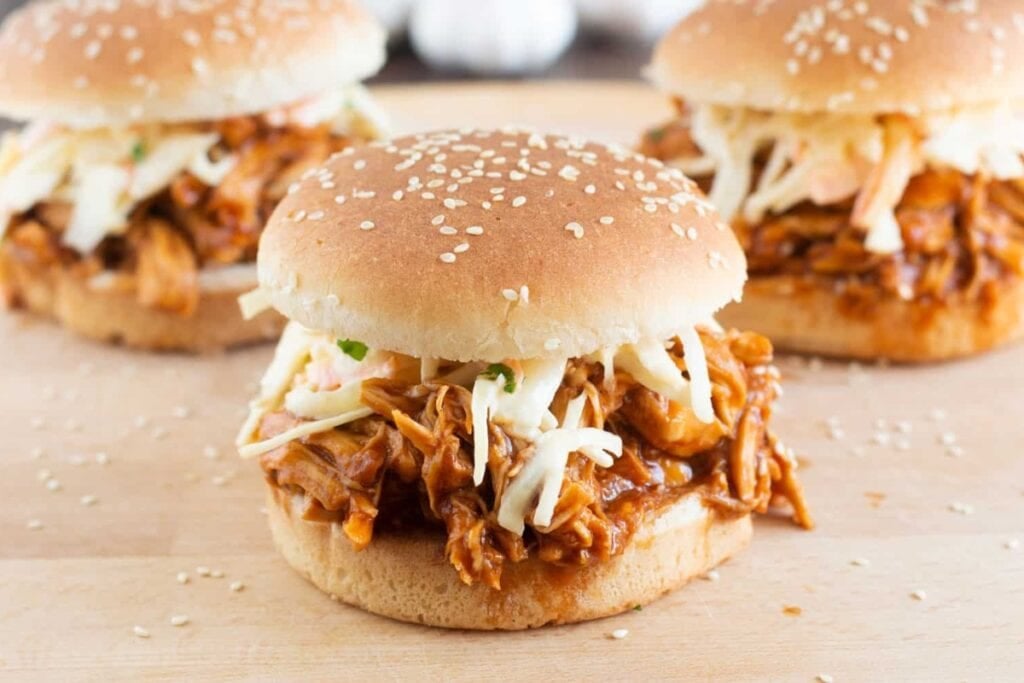 Crockpot BBQ chicken in buns on a wooden board.