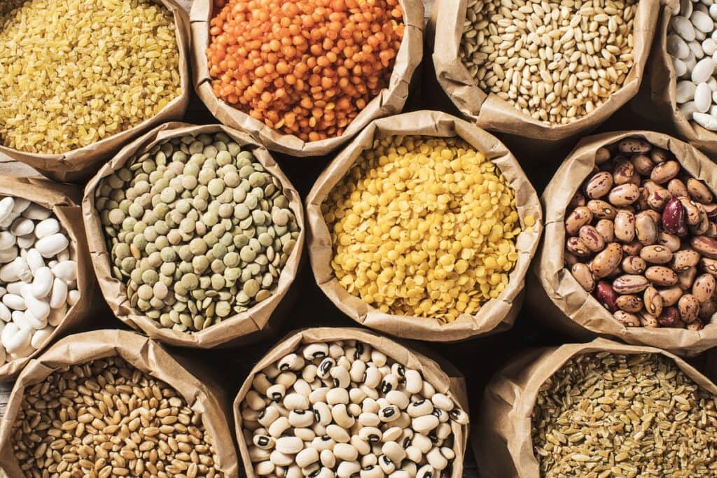Variety of legumes packed in brown paper bags on display.