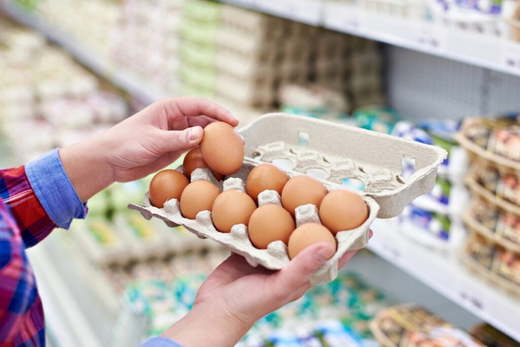 Person holding a tray of eggs in a grocery store.