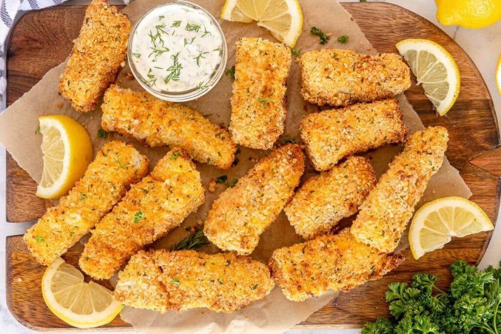 Fish sticks on a wooden board with dipping sauce.