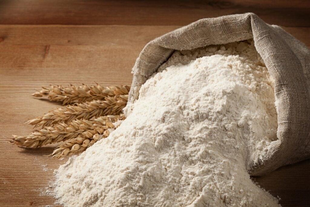Sack of flour on wooden surface with wheat stalks.