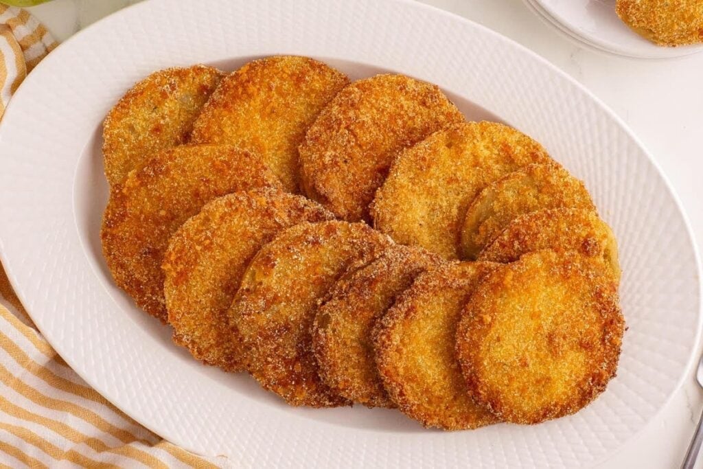 Golden brown fried green tomatoes arranged on a white oval plate.