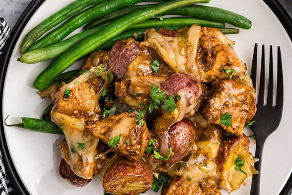 Garlic Parmesan chicken, potatoes, and green beans served on a white plate with a fork on the side.