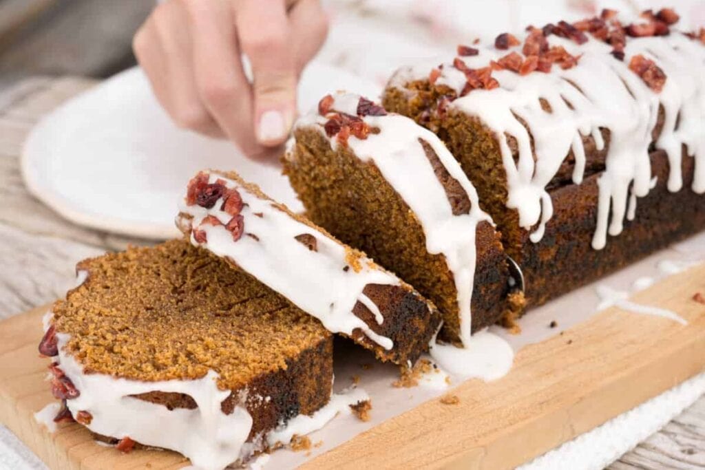 Slicing gingerbread loaf cake on a wooden board.